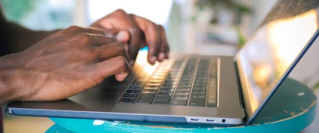 Close-up of hands typing on a laptop keyboard placed on a blue stool indoors