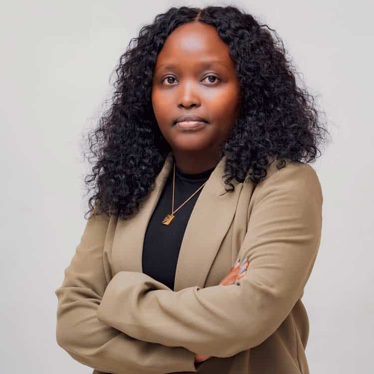 Wangui Mukono, Compliance Director at ARC Power, smiling confidently in a dark green blazer with arms crossed, photographed against a light studio background.