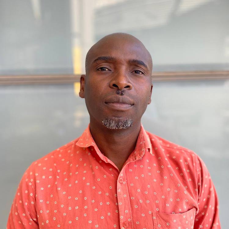Emmanuel Chilufya, Establishment Manager at ARC Power, wearing a coral button-up shirt with a subtle pattern, standing in front of a frosted glass background.
