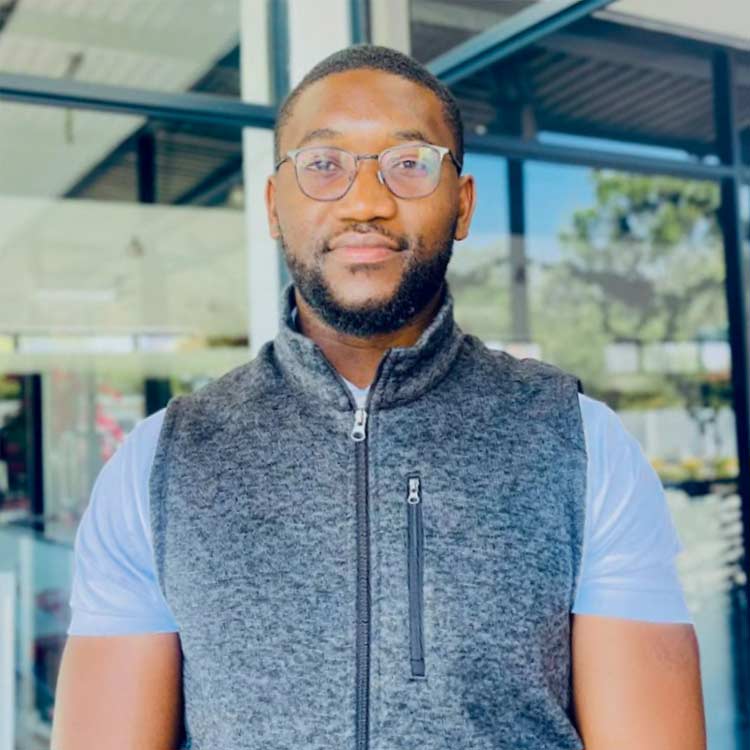 Moono Longwani, Assets and Procurement Assistant at ARC Power, wearing glasses and a grey zip vest, standing in front of a glass building.