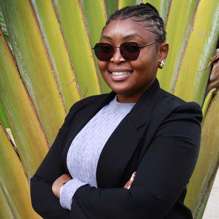 Jennifer Novela, Systems Manager at ARC Power, smiling confidently with arms crossed, wearing sunglasses and a black blazer, standing in front of large tropical leaves.